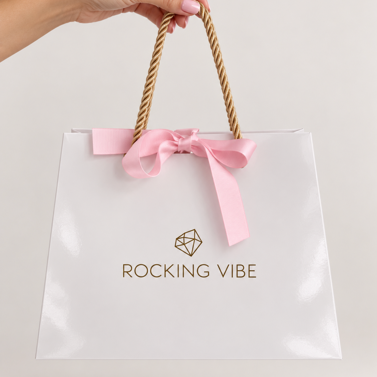 ROCKING VIBE signature gift bag in high-gloss white with gold rope handles and pink silk ribbon