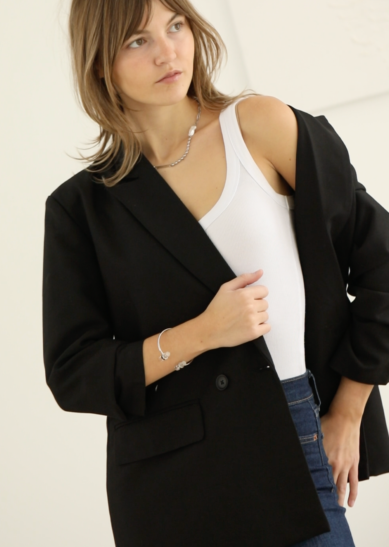 Woman wearing a black blazer over a white top and blue jeans on a plain background