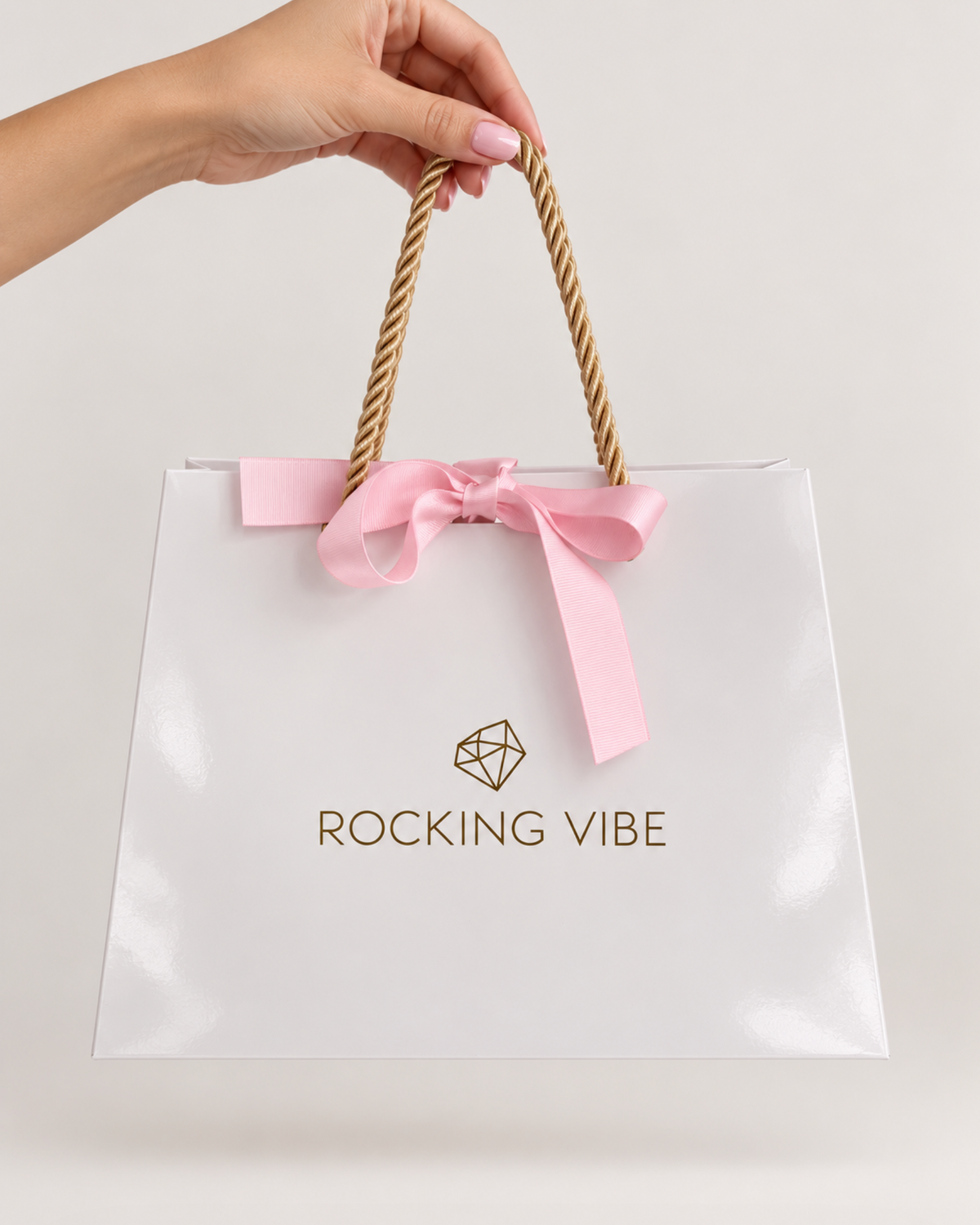 ROCKING VIBE signature gift bag in high-gloss white with gold rope handles and pink silk ribbon