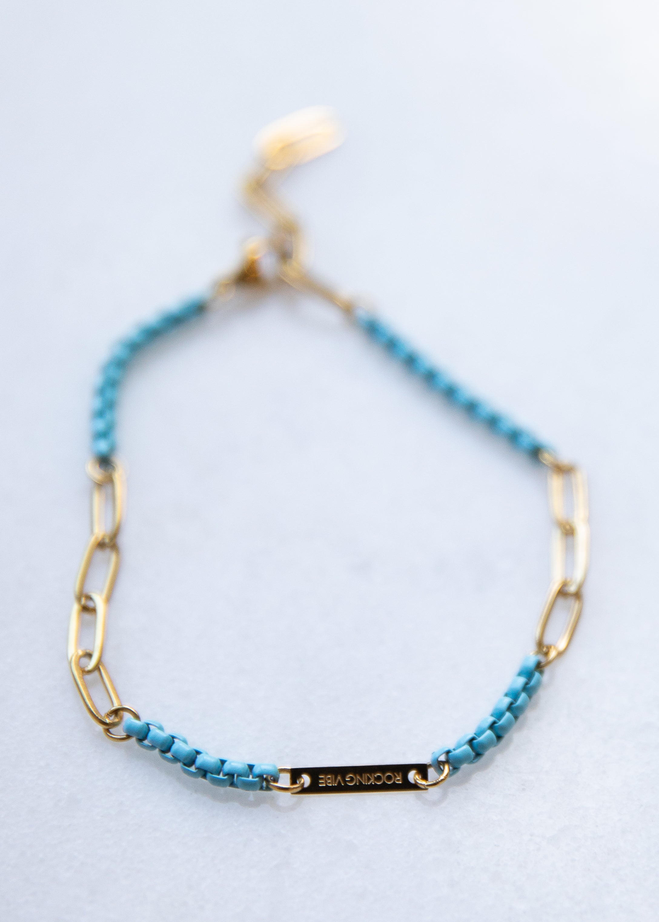 Turquoise beaded bracelet with gold chain on a light gray background