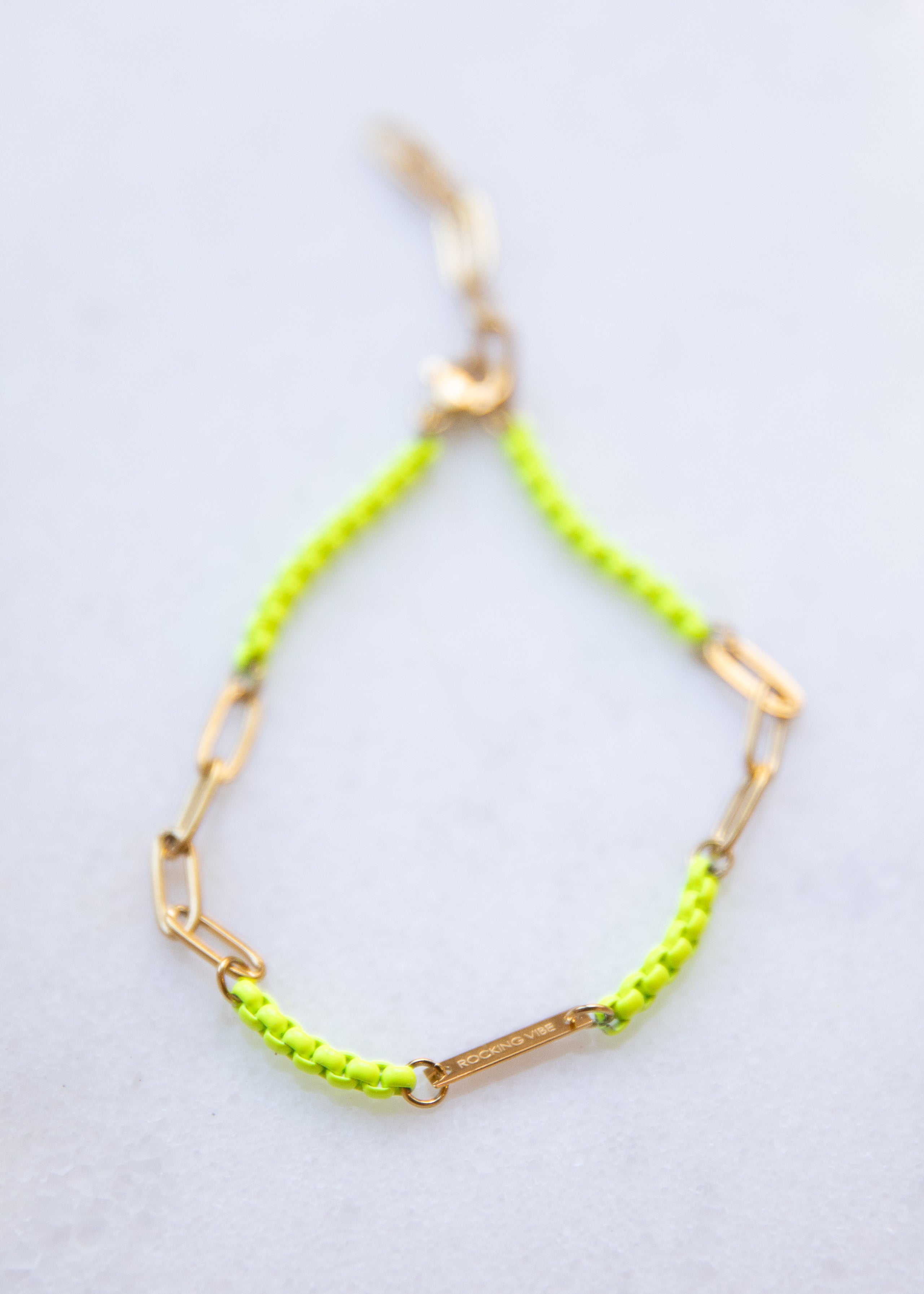 Neon yellow bracelet with gold chain on a white background