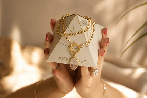 Hands holding the Rocking Vibe Intention Pyramid with a gold necklace draped over it